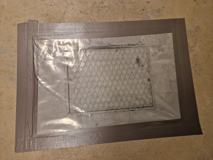 Ventilationsgaller täckt med plastfolie och tejpad kant på ett betonggolv. Reparation eller skyddsåtgärd.
