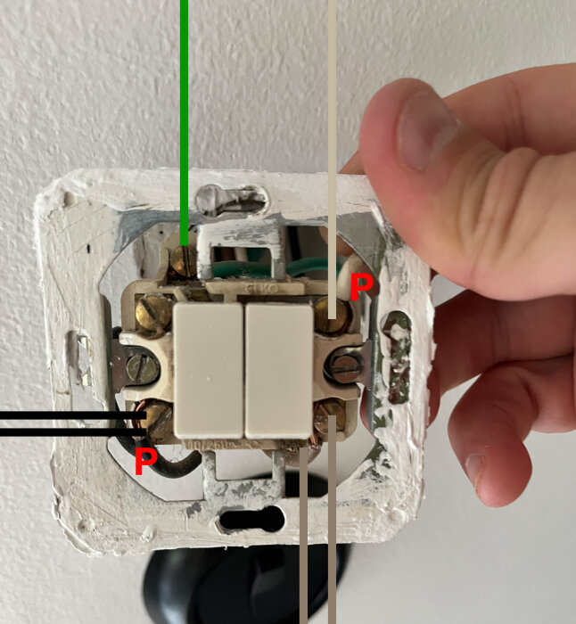 En hand vidrör en delvis demonterad ljusströmbrytare med synliga ledningar och spackel på väggen.