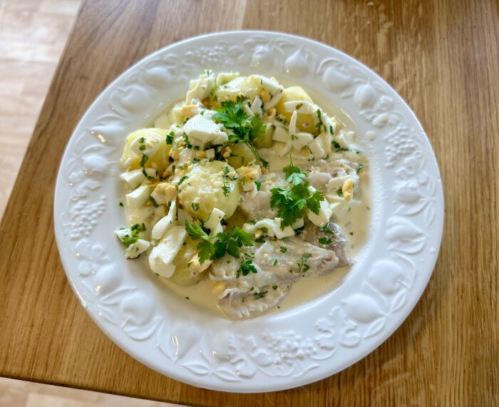 Fiskrätt med potatis, sås, ägg, persilja på dekorerad tallrik och träbord.