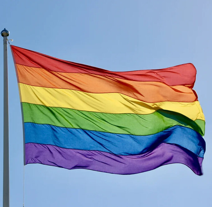 Regnbågsflagga vajar mot klar himmel, symbol för LGBTQ+ gemenskap och mångfald.