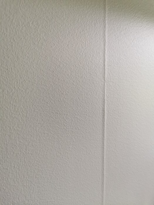 Vit texturerad vägg med ett hörn, ljusskuggning, minimalistiskt, inomhus miljö.