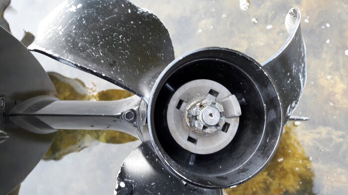 Bild pÄ en skadad bÄtmotorpropeller ovanför vatten, med vattendroppar och tydliga bruksspÄr.