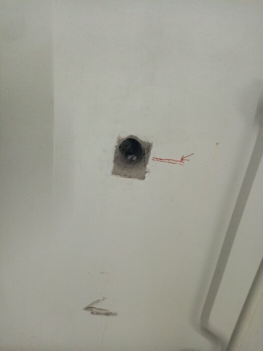 Ett hål i en vit vägg med röd markering och några mindre skador.