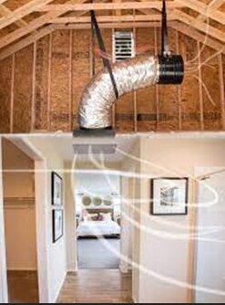Loftutrymme med synliga takbjälkar, ventilationssystem; sovrum nedanför med säng och tavlor på väggen.