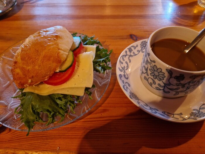 Ett smörgås med ost och grönsaker och en kopp kaffe på ett träbord.