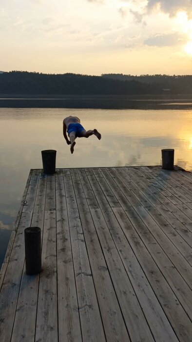 Person gör en bakåtvolt från en brygga in i en sjö vid solnedgången.