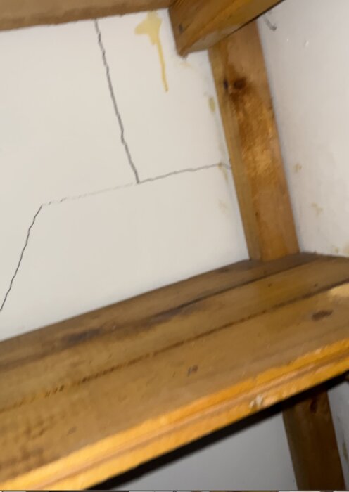 Vit vägg med sprickor, träbjälkar och fläckar, strukturproblem, behov av reparation.