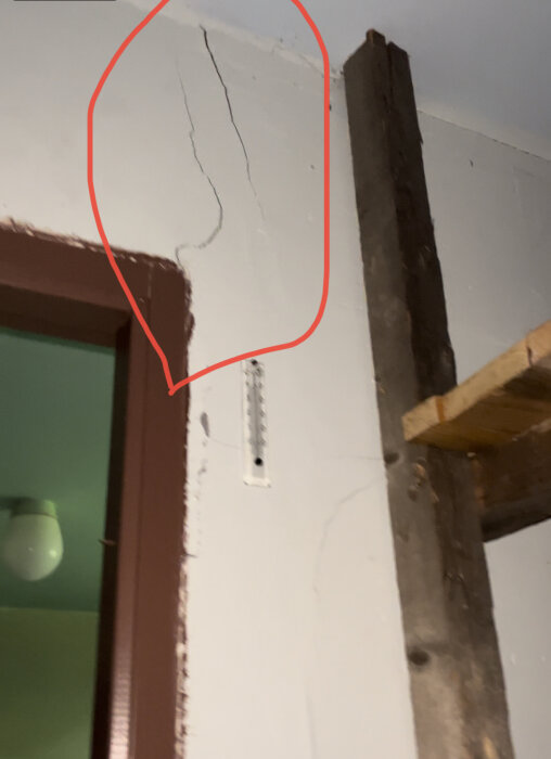 Inomhusmiljö med sprickor i vägg, träbjälke, termostat och en grön lampskärm; tecken på underhållsbehov.