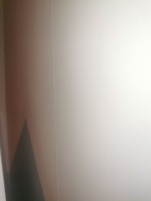 En vit vägghörna med en mörk triangel av skugga nedtill. Minimalistisk, enkel och abstrakt med mjuk belysning.