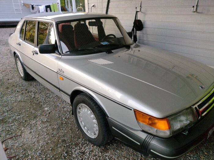 Silverfärgad klassisk Saab Turbo parkerad på grus vid ett hus.