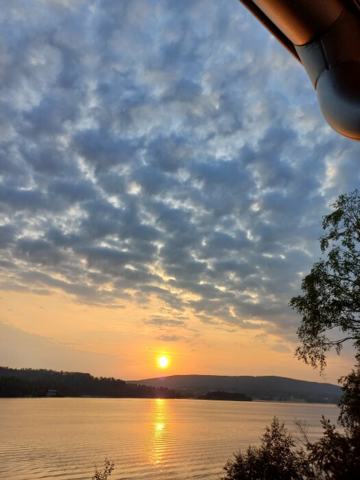 Solnedgång över en sjö, molnbeströdd himmel, reflektion i vattnet, natur, avkopplande vy.