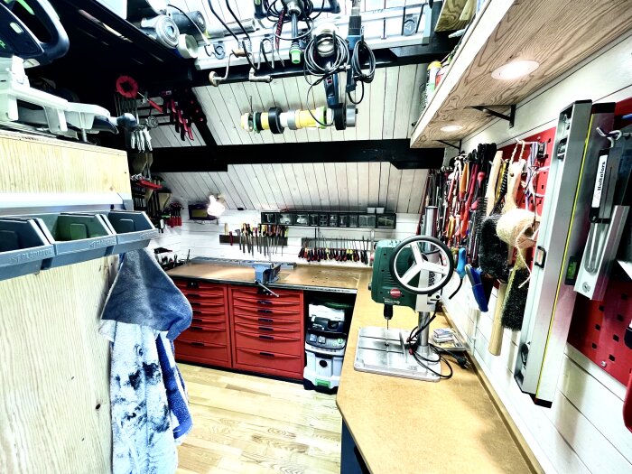 Välorganiserad verkstad med verktygstavlor, röda verktygsskåp och en bänkborrmaskin på arbetsbänk.