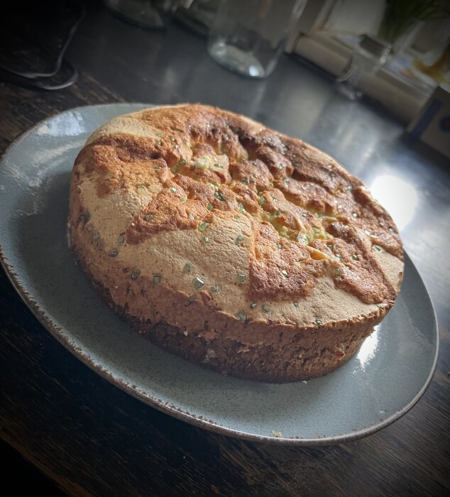 Hembakad kaka på tallrik med strösocker, rustikt köksbord i bakgrunden.