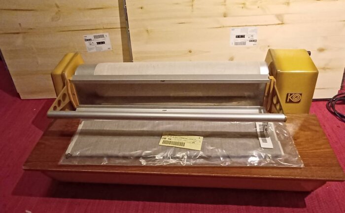 Bord med oöppnad förpackning, byggsatsdelar, träbakgrund, golvkabel, gul konstnärsattribut och röd matta.