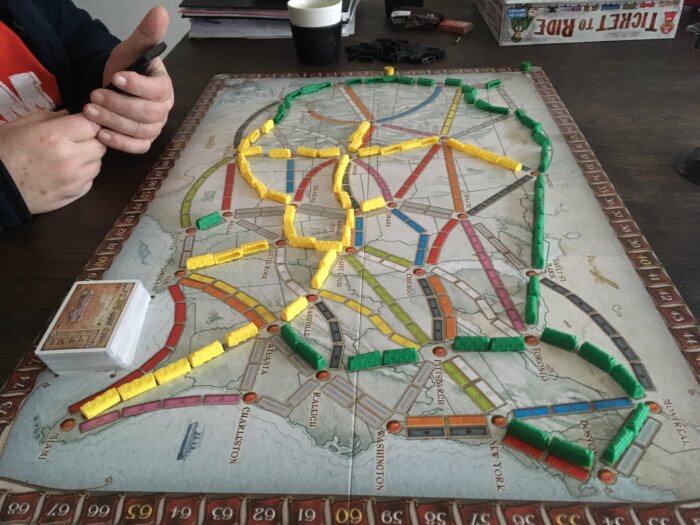 Ett brädspel av "Ticket to Ride" med tågvagnar på en spelplan, samt kort och en persons hand.