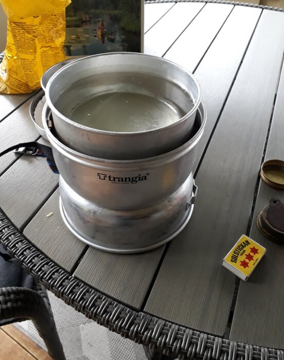 Trangia stormkök med kastrull pÄ bord, tÀndstickor, utomhussituation, matlagning, camping, vandring, Àventyr, friluftsliv.