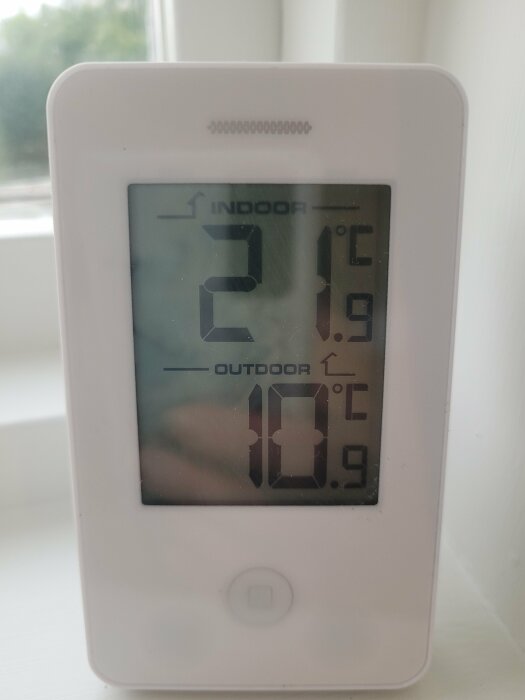 En digital termometer som visar inomhus- och utomhustemperatur på en vit bakgrund.