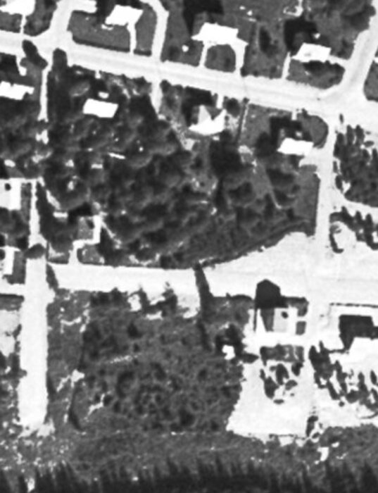 Svartvit översiktsbild, troligen satellitfoto, visar bebyggelse, vägar, och vegetation med låg upplösning.