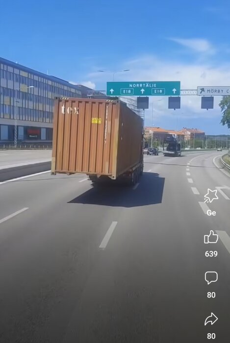 Container på lastbil, vägskyltar med destinationer, klar himmel, möjlig trafiksituation, dagtid.