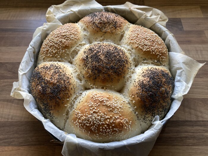 Nybakat bröd i form, toppat med sesam- och vallmofrön, på ett träbord.