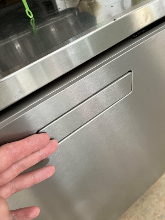 En hand öppnar en rostfri ståldörr till en modern köksutrustning, möjligtvis en diskmaskin.