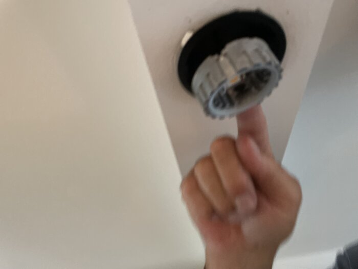 En hand som rör vid en borttagen rökdetektor på ett suddigt foto.