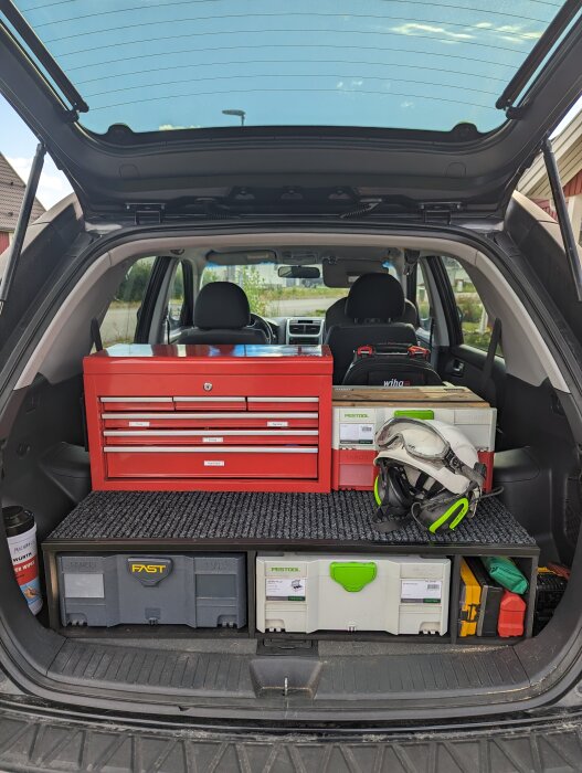 Bilens bagageutrymme fyllt med verktygslådor, en verktygsvagn och skyddsutrustning; organiserat för arbete.