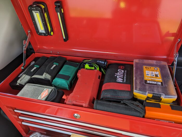 Röd verktygslåda med mångsidiga verktyg och organiseringsetuier, inklusive skruvmejsel och mätverktyg.