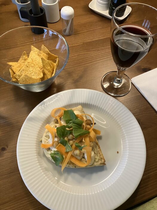 Middagsdukning med mat, vin, chips, kryddor, modern enkel inredning.