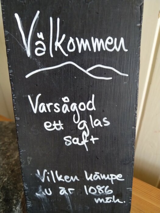Svart tavla med vit text på svenska, inbjuder till ett glas saft och frågar om vandringslängd.