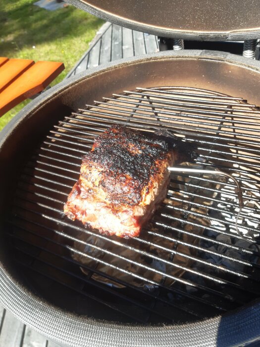 Ett stekt köttstycke på en grill utomhus under solig dag.