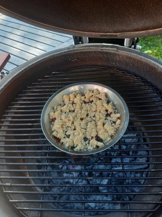 Ett metallfat med mat ovanpå en glödbädd i en öppen grill.
