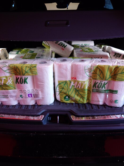 Bagageutrymme fullt med köks- och toalettpappersrullar. Bilens baklucka öppen. Städprodukter efter storhandling.