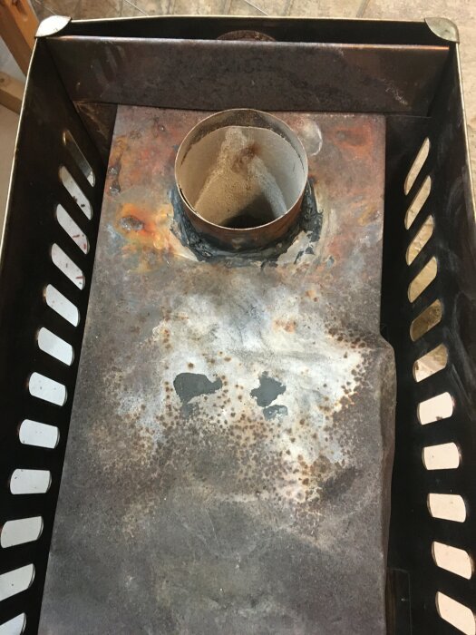 Rostigt, metalliskt föremål med cylinderformat objekt, slitna ytor, fläckar och mönstrade utsågningar.