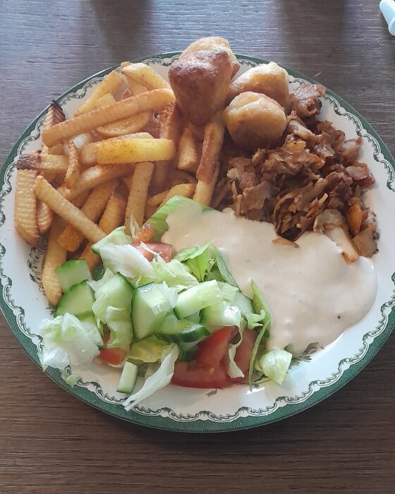 En tallrik med mat; pommes, kött, sallad, sås och friterade bollar.