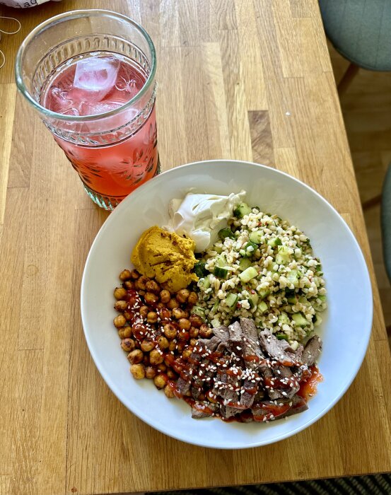 Maträtt med stekt kött, kryddiga kikärtor, sallad, pumpakräm, gräddfil, sesamfrön och en iskall röd dryck.