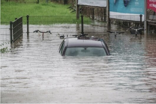 En bil översvämmad med vatten, inhägnad och vägskylt synliga, potentiellt efter kraftigt regn eller översvämning.