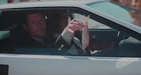 Två personer i en bil, en man kör, ger pengar genom öppet fönster.