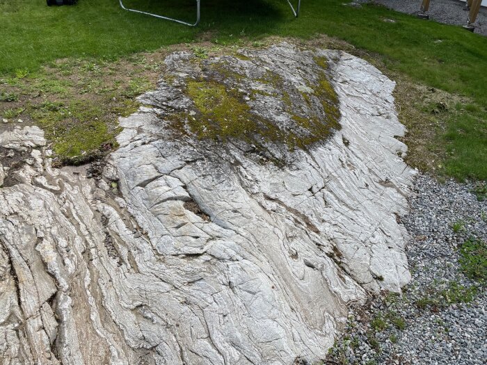 Stor sten i gräsmatta, mossa, grusväg, texturrik yta.