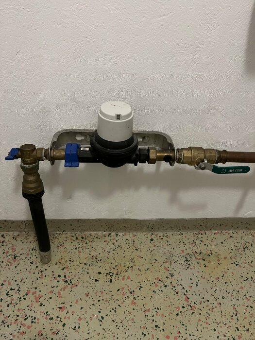 Vattenmätare med avstängningsventiler och kopplingar monterad på vägg och golv.