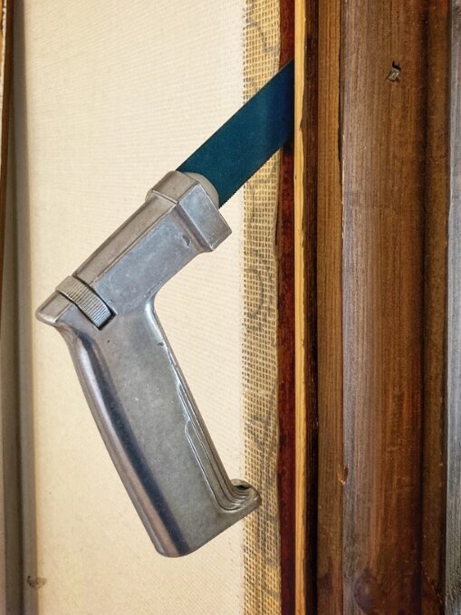 Kniv fastklämd i springan mellan en dörr och karmen, med metallhandtag synligt.