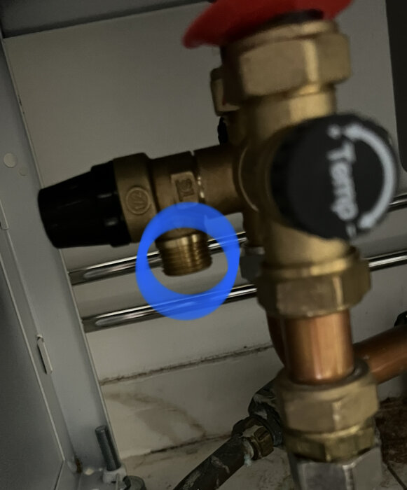 Rörkoppling med blå ringmarkerad detalj, röd ventil och svart spak under skåp. Fokus på koppling.