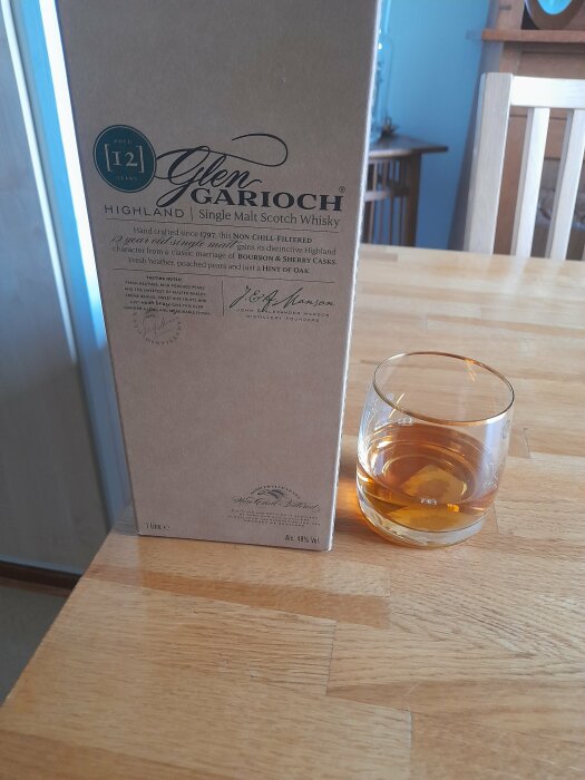 Flaska Glen Garioch 12-årig single malt Scotch whisky och ett glas med whisky på träbord.