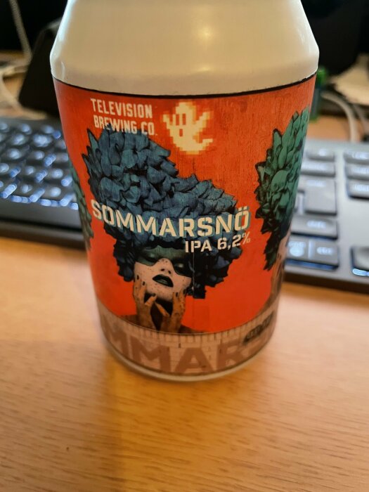 En ölburk med etikett "Sommarsnö IPA", tangentbord i bakgrunden.