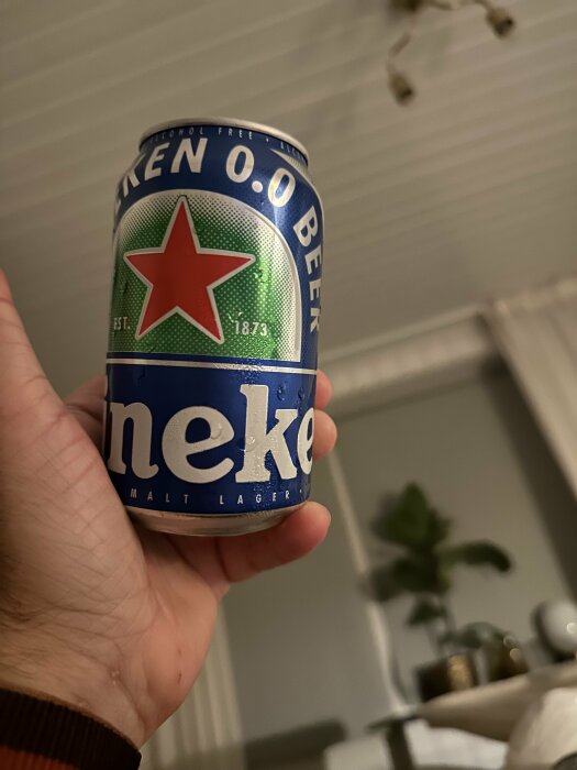 En hand håller en burk alkoholfritt öl med etikett och röd stjärna, inomhusmiljö.