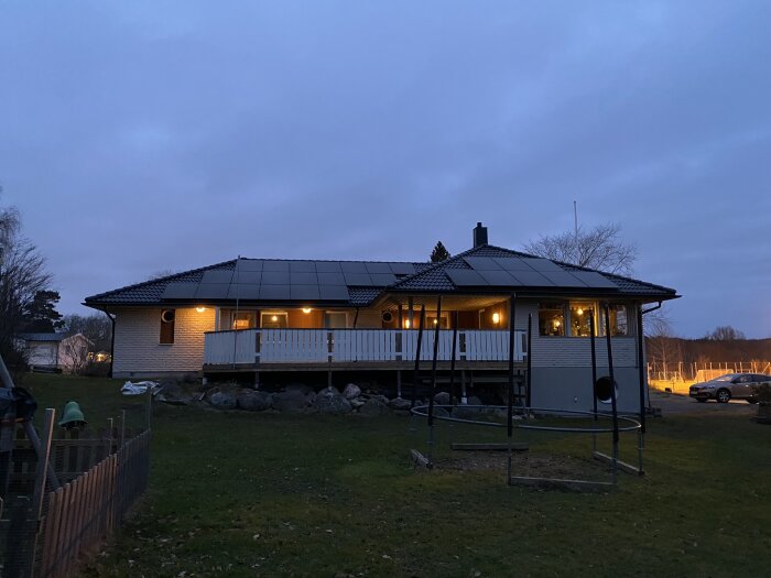 Ett hus vid skymningen, belyst veranda, takpannor, bil, gräsplätt, inget snö.