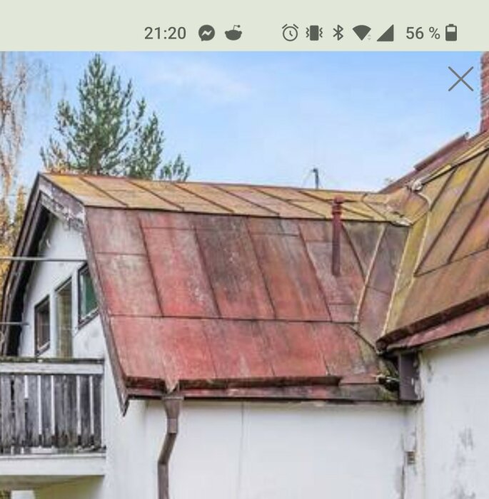 Ett hus med slitet koppartak och balkong mot en himmel med träd.