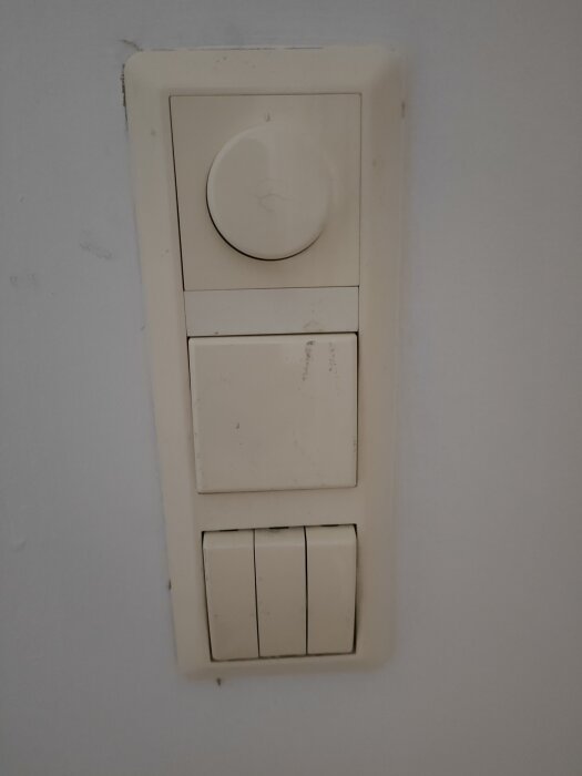 Vit väggmonterad strömbrytare kombinerad med dimmer, ser använd och lite smutsig ut.