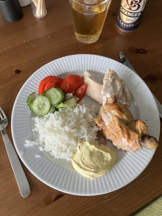 Måltid med ris, grillad kyckling, grönsaker, sås, och öl. Enkel hemlagad middag på matbordet.