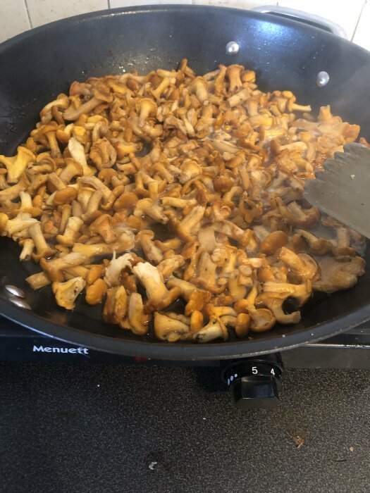 Stekpanna med sauterade kantareller på en spis. Matlagning, svamp, köksredskap.